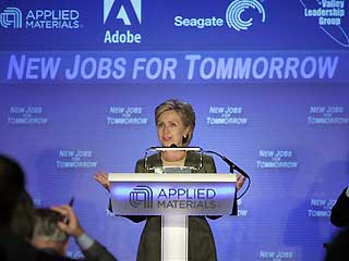 Hillary Clinton standing behind a podium, with a banner behind her that says “Jobs for Tommorrow”