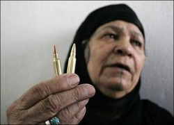 A older woman in a black head scarf holds up two bullets, still in their casings